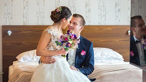 Hochzeitspaar sieht sich verliebt an und sitzt auf dem Bett
