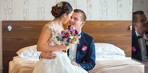 Hochzeitspaar sieht sich verliebt an und sitzt auf dem Bett